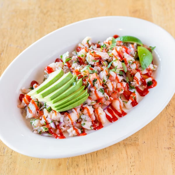 El Chubasco's shrimp ceviche with avocado slices, lime wedges, and red sauce on a white plate.