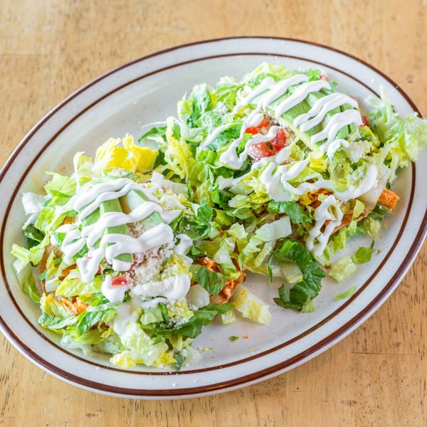 Two El Chubasco tostadas topped with shredded lettuce, avocado, sour cream, and cotija cheese.