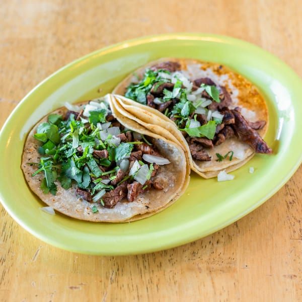 Two El Chubasco carne asada tacos with cilantro and onions on a bright green plate.