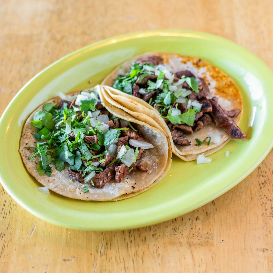Two El Chubasco carne asada tacos with cilantro and onions on a bright green plate.