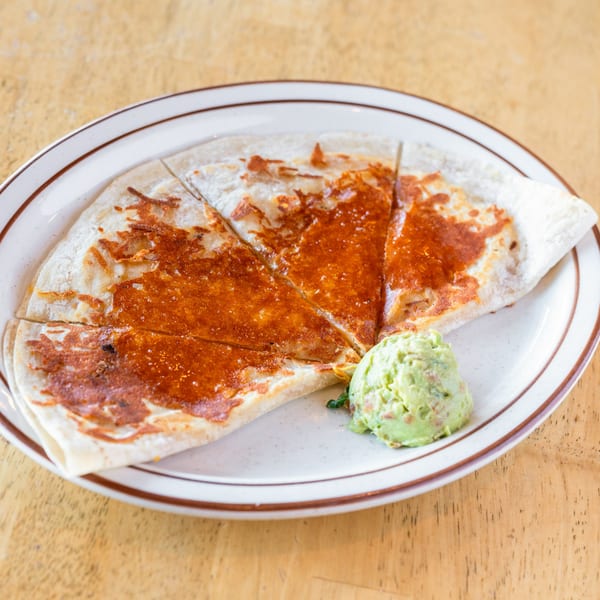 A cheese quesadilla, cut into triangles, with a scoop of guacamole on a white plate.