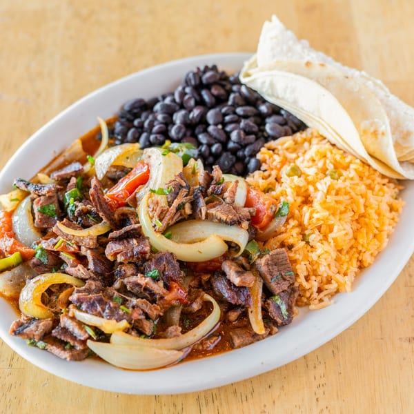 El Chubasco's carne asada with onions, peppers, rice, black beans, and tortillas on a white plate.