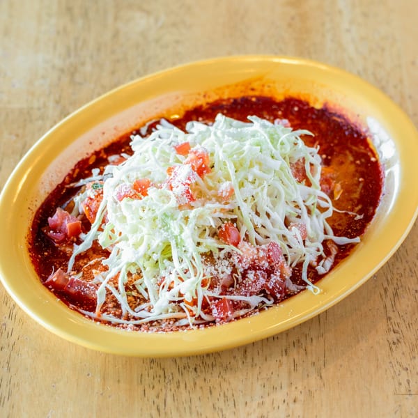 El Chubasco's Mexican dish with red sauce, shredded cabbage, diced tomatoes, and cheese on a yellow plate.
