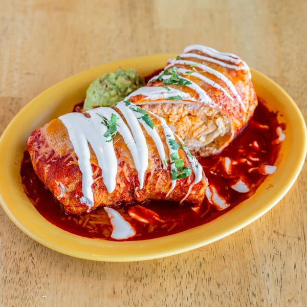 Two El Chubasco burritos, one cut open, covered in red sauce, sour cream, and cilantro, with guacamole.